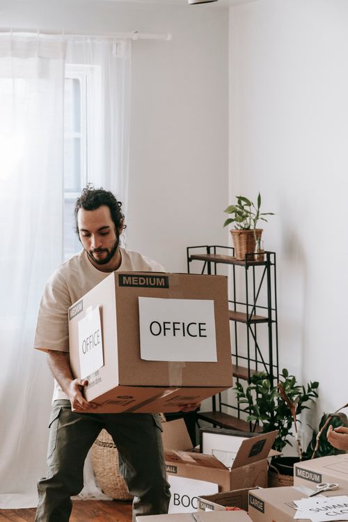 Hombre joven cargando una caja de cartón etiquetada durante una mudanza empresarial